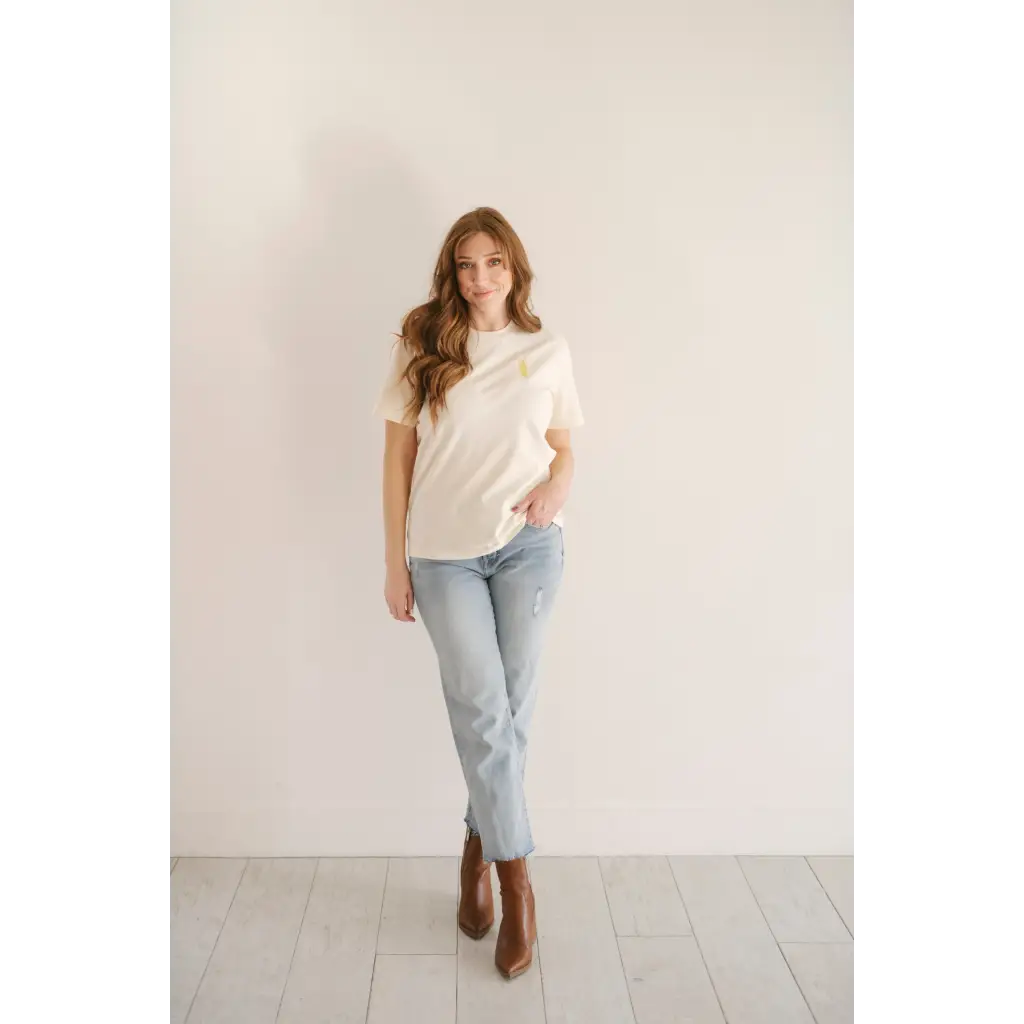 Person in white vibes peace embroidered tee, light blue jeans, and brown ankle boots