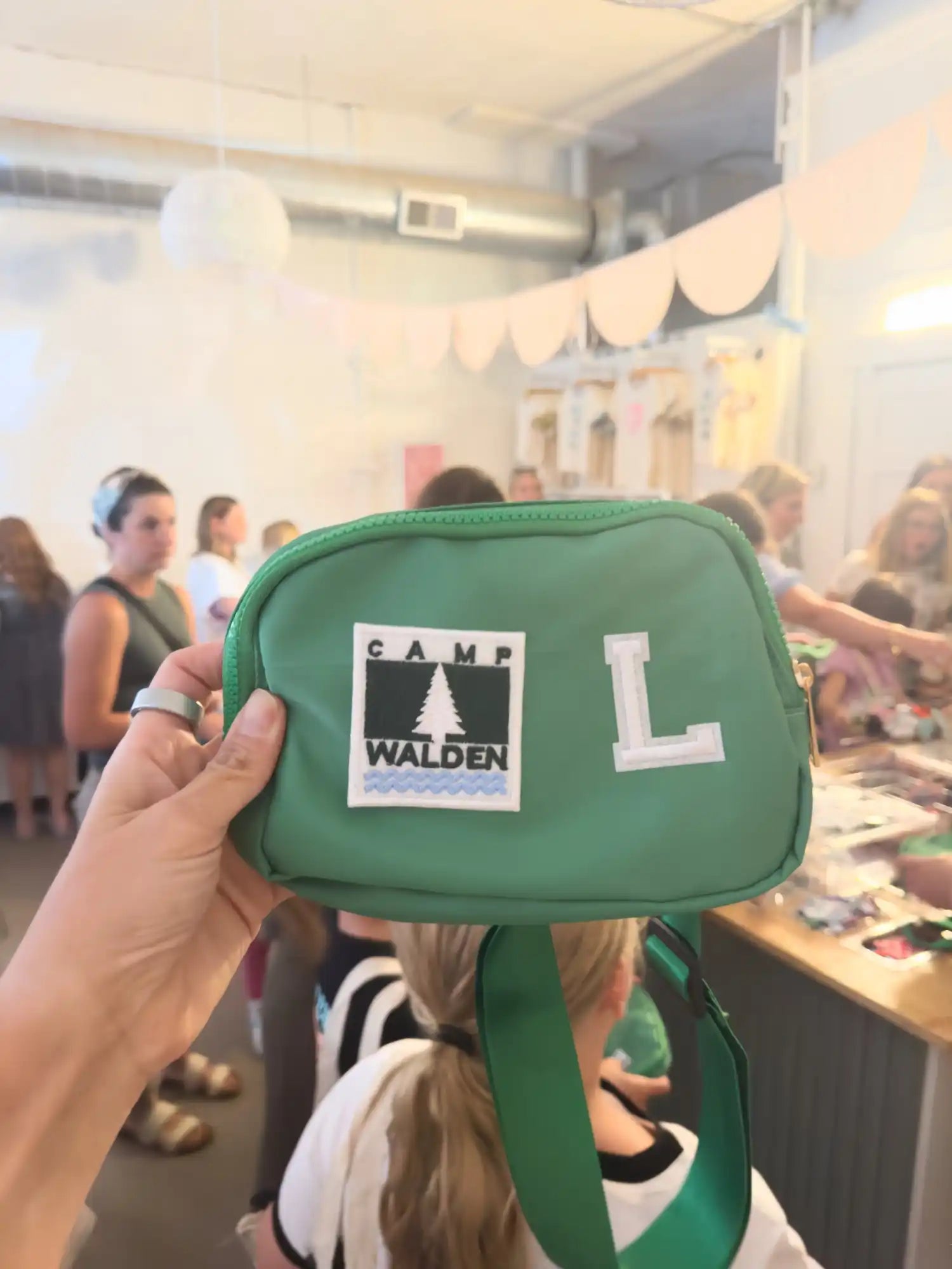 Green rectangular pouch with a white letter ’L’ and a ’Camp Walden’ patch.