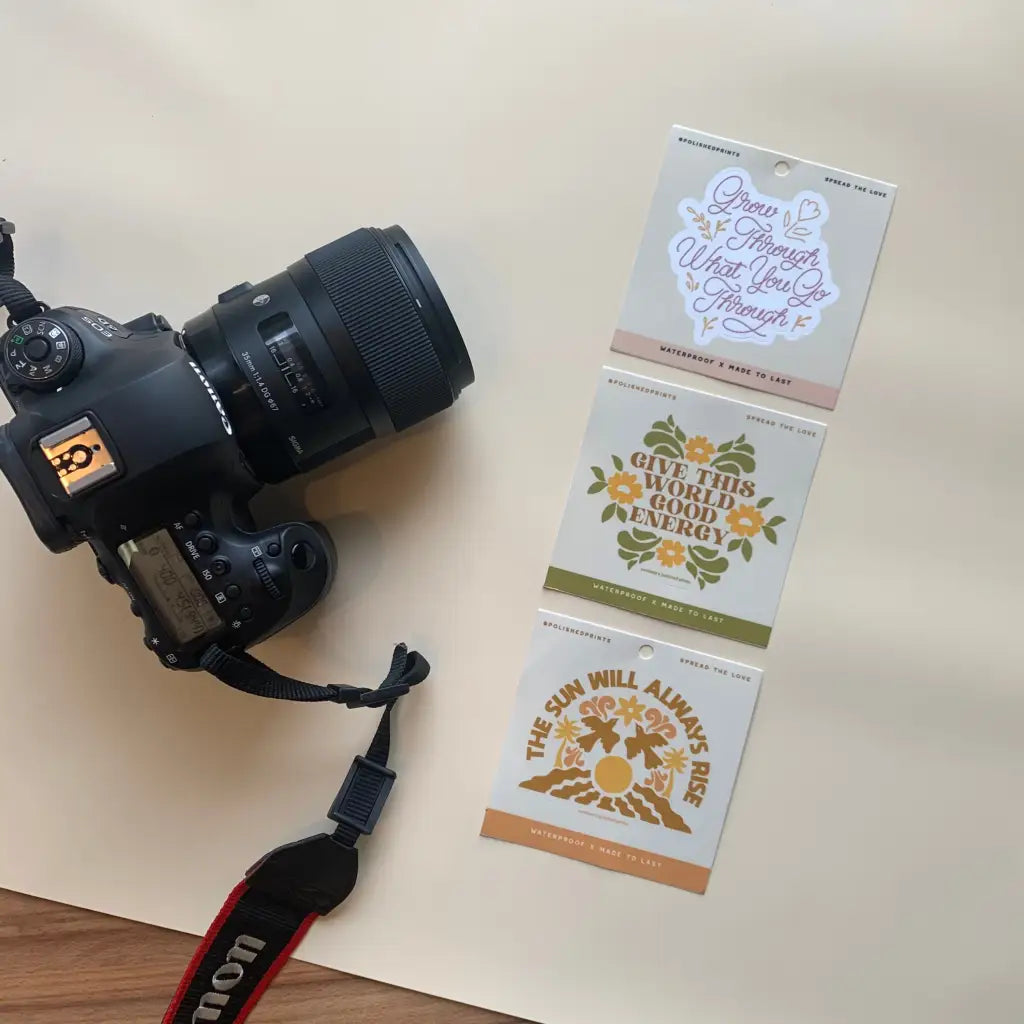 Black Sony camera with zoom lens next to a waterproof sticker with positive message inspiring growth