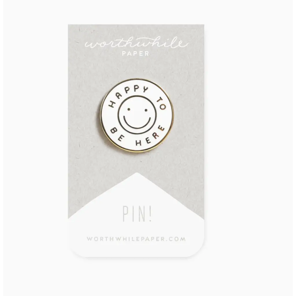 Circular white enamel pin with smiley face and HAPPY TO BE HERE text for present moment