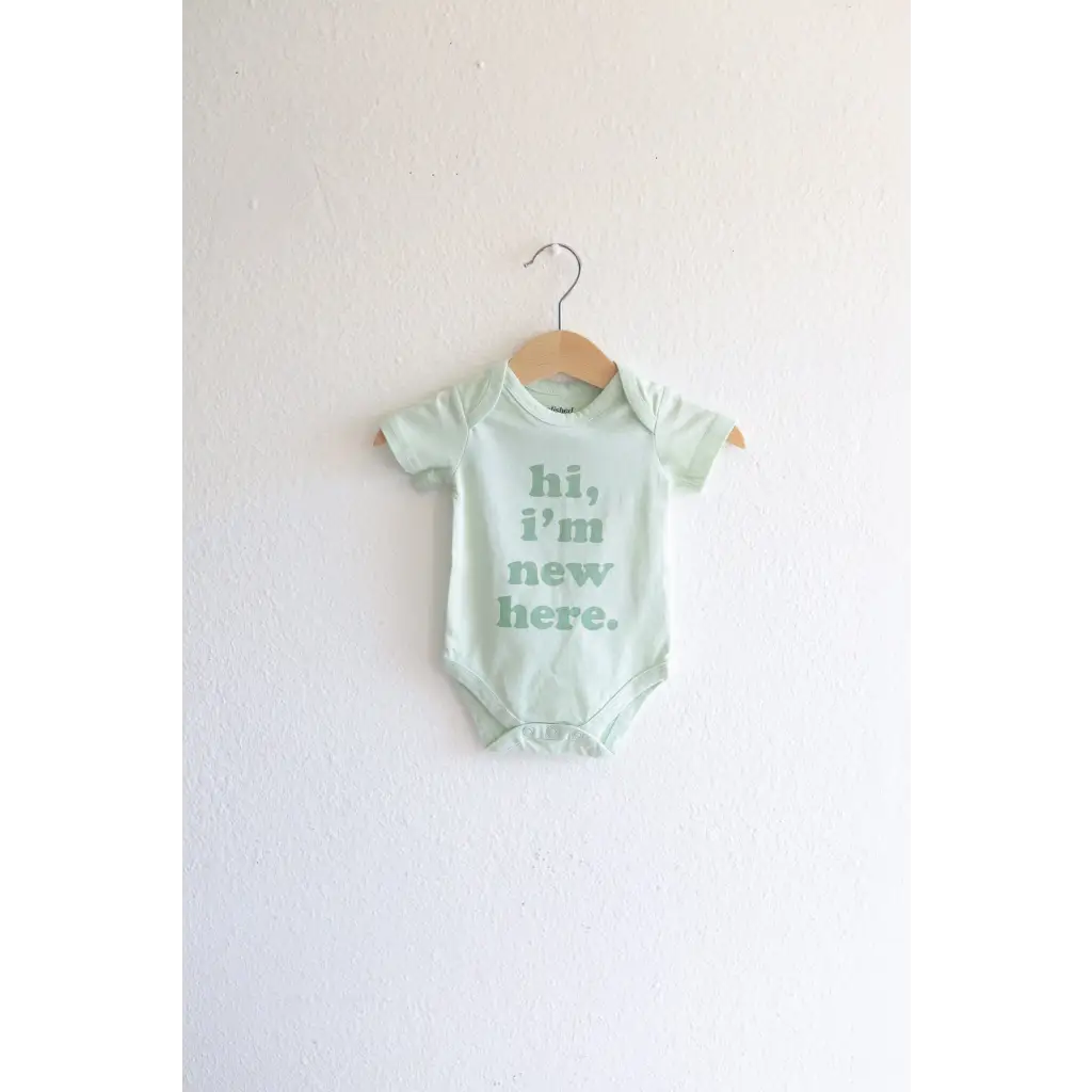 Mint green organic cotton baby onesie with hi, I’m new here text on wooden hanger