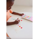 Young kid with dark skin coloring in Ice Cream Pocket Watercolor Book at a white table