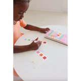 Young kid with dark skin coloring in Ice Cream Pocket Watercolor Book at a white table