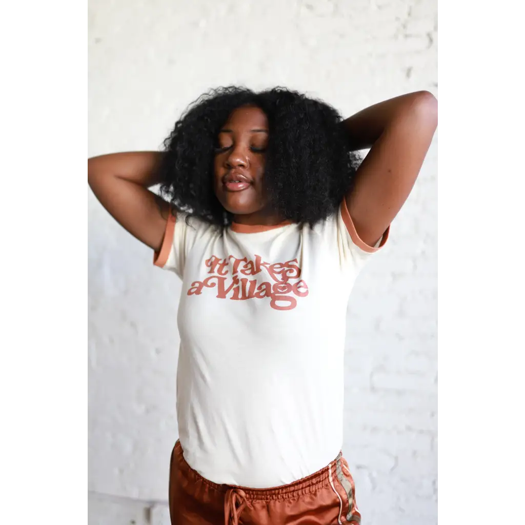 Person in a white graphic Adult Retro Ringer Tee and rust pants, rocking curly hair