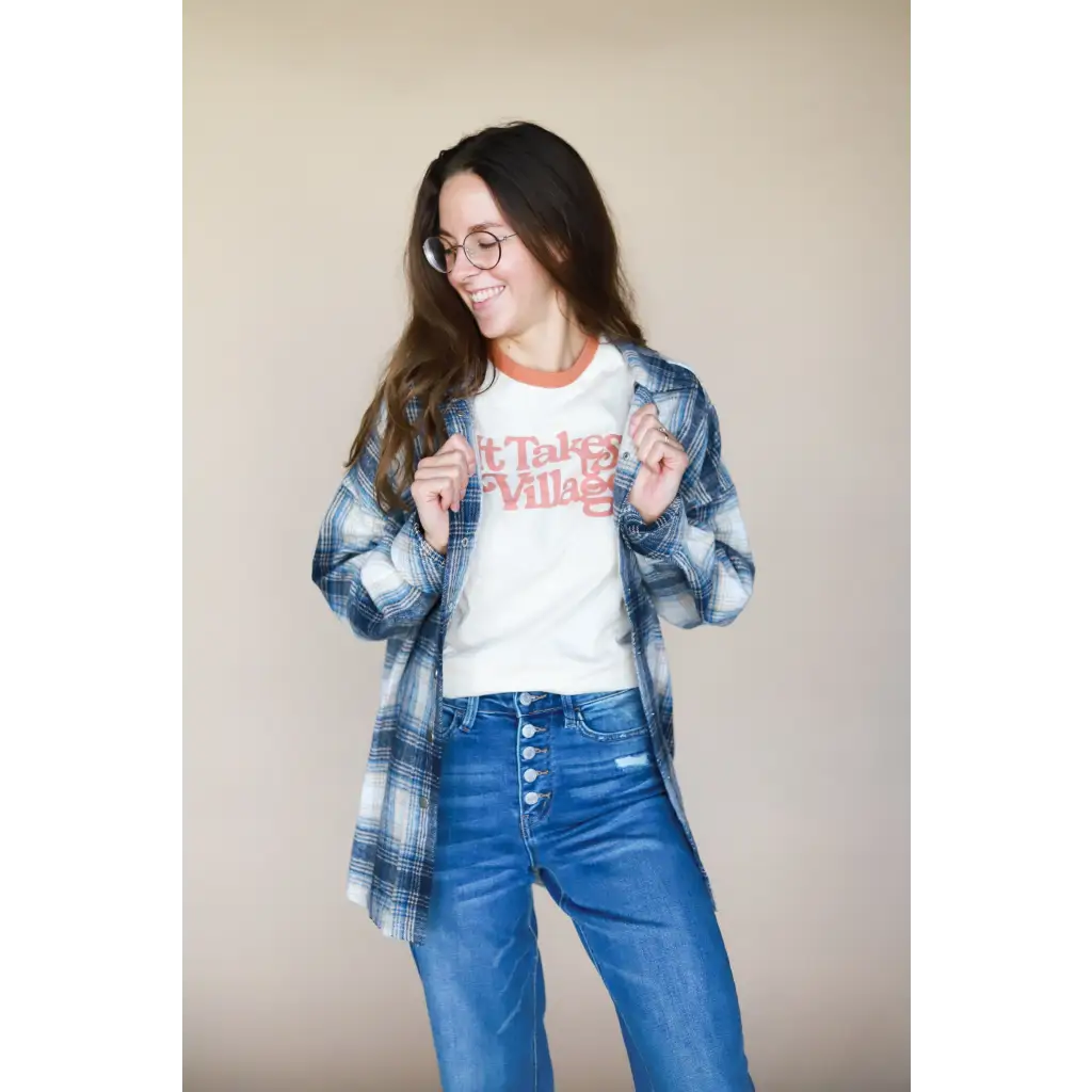 Person in plaid flannel and blue jeans, showcasing It Takes a Village Adult Retro Ringer Tee