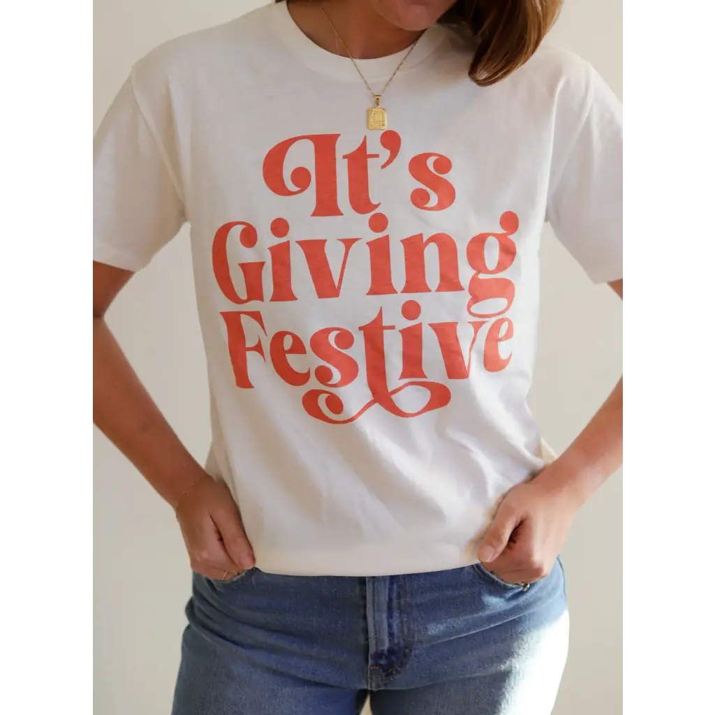 White Giving Festive Unisex T-shirt featuring coral text that says It’s Giving Festive