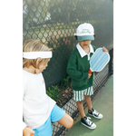 Two kids in sneakers by a fence showing off their mini pickle ball paddles