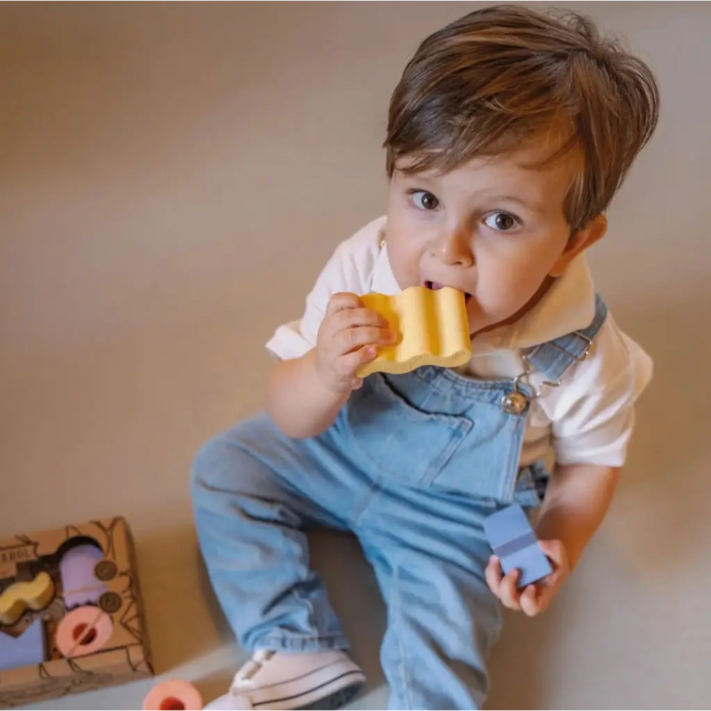 Young child in denim overalls enjoying bread with Floating Stacking Blocks in Natural Rubber
