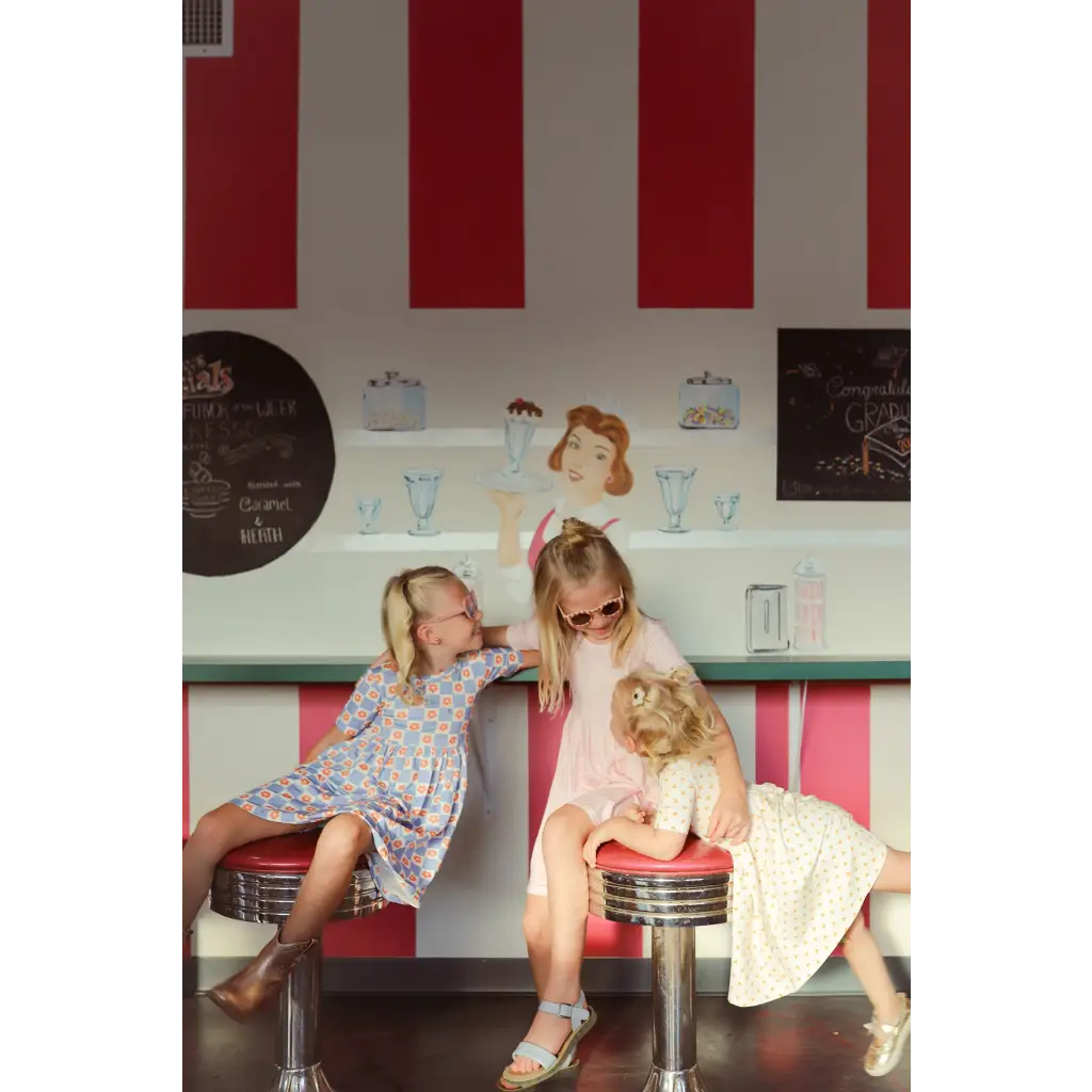 Three kids enjoying playtime in a retro diner while wearing a cute Day Twirl Dress