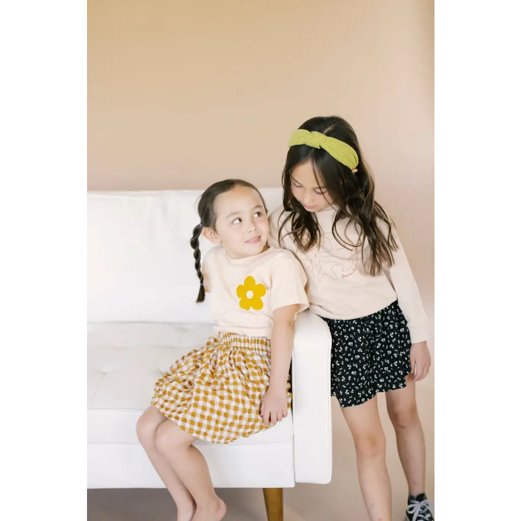 Two kids in patterned skirts on a chair, wearing love grow graphic t-shirts