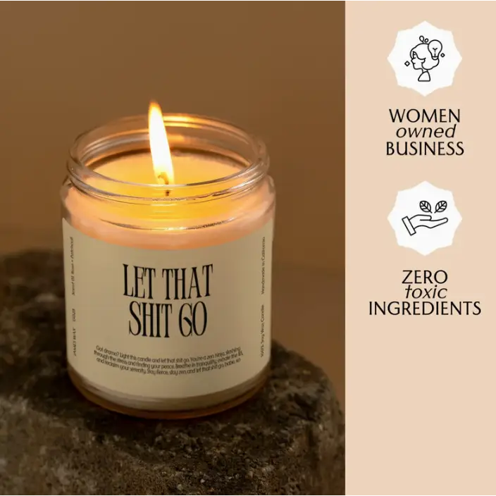 Lit candle in jar with Let That Shit Go label, creating small batches of rose + patchouli vibes