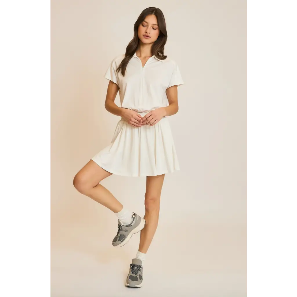 Woman in a white polo shirt and skirt modeling the Libby Athletic Mesh Romper with Front Zip