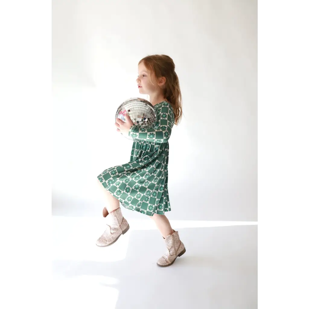 Young child in green dress holding disco ball, featuring Lily Flower Check design