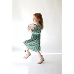 Young child in green dress holding disco ball, featuring Lily Flower Check design