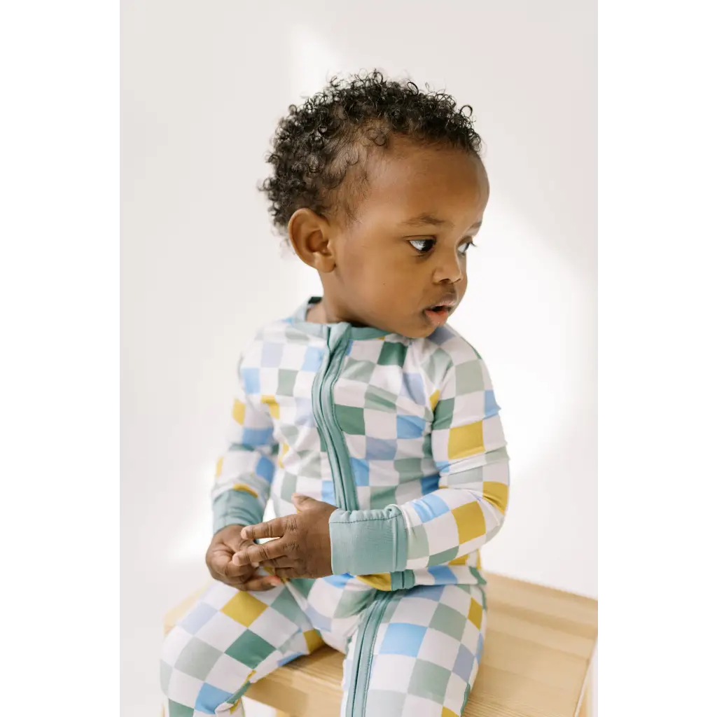 Child in a pastel checkered jumpsuit from Little Houses Bamboo Baby Sleeper