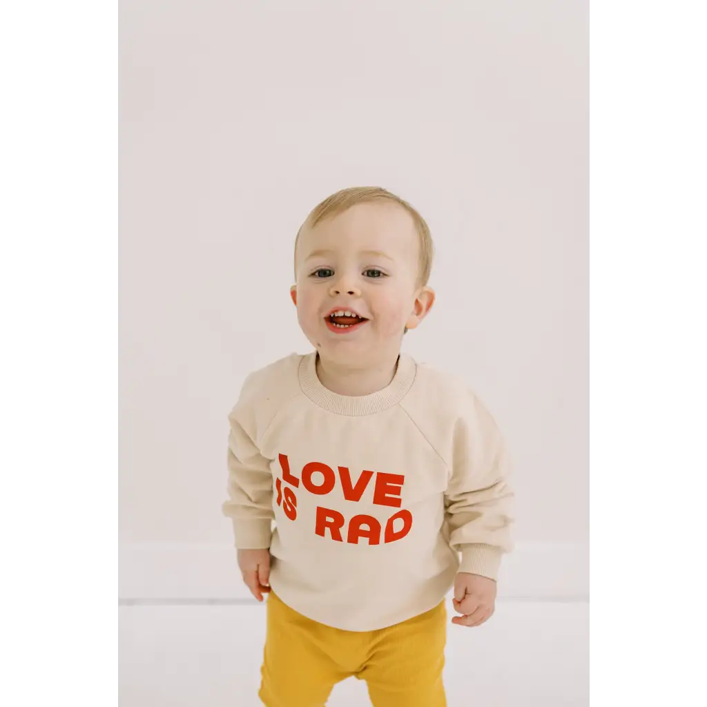 Smiling toddler in Cream Love is Rad Baby Pullover made of organic cotton fabric