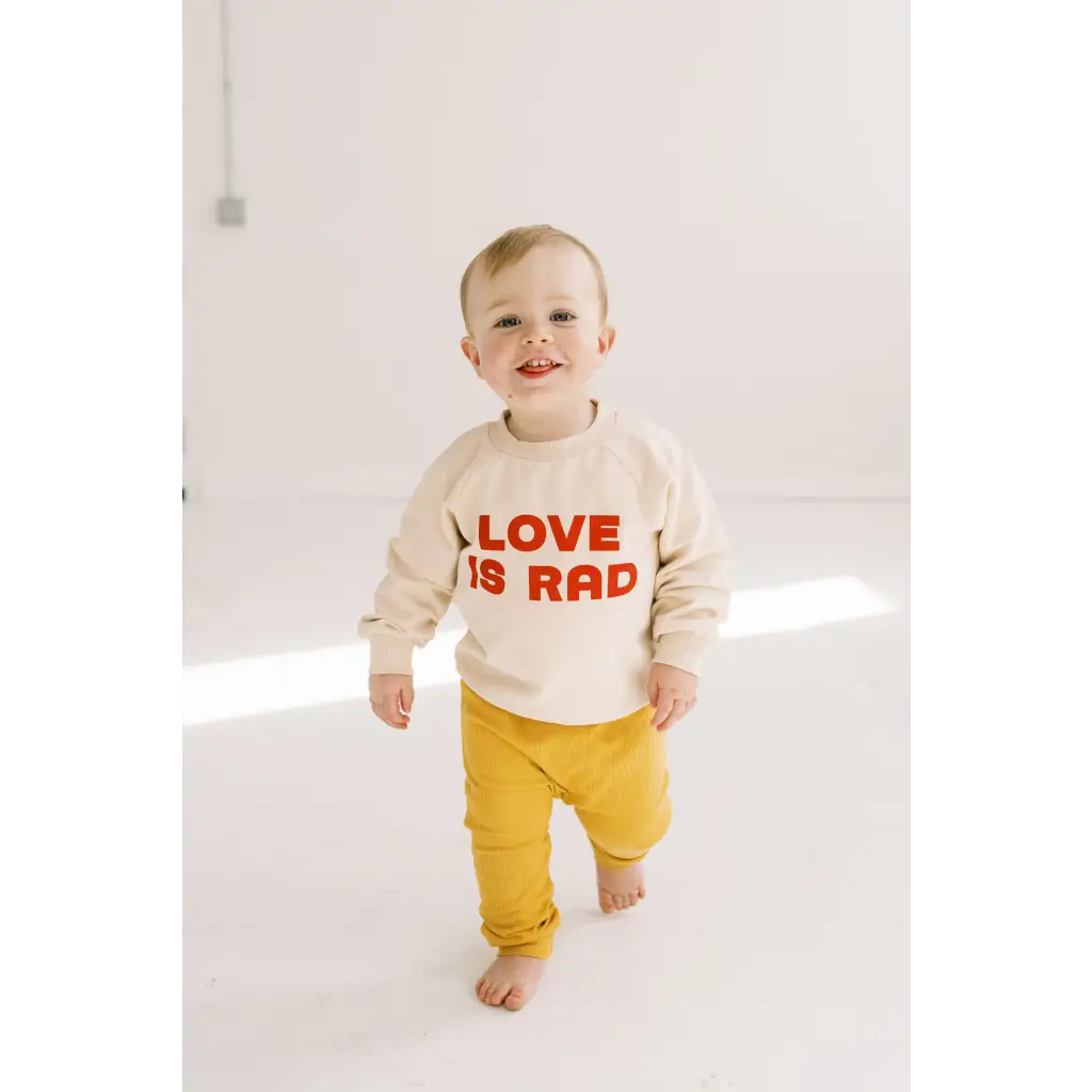 Toddler in cream Love is Rad sweatshirt and yellow pants, rocking a Rad Kids Pullover