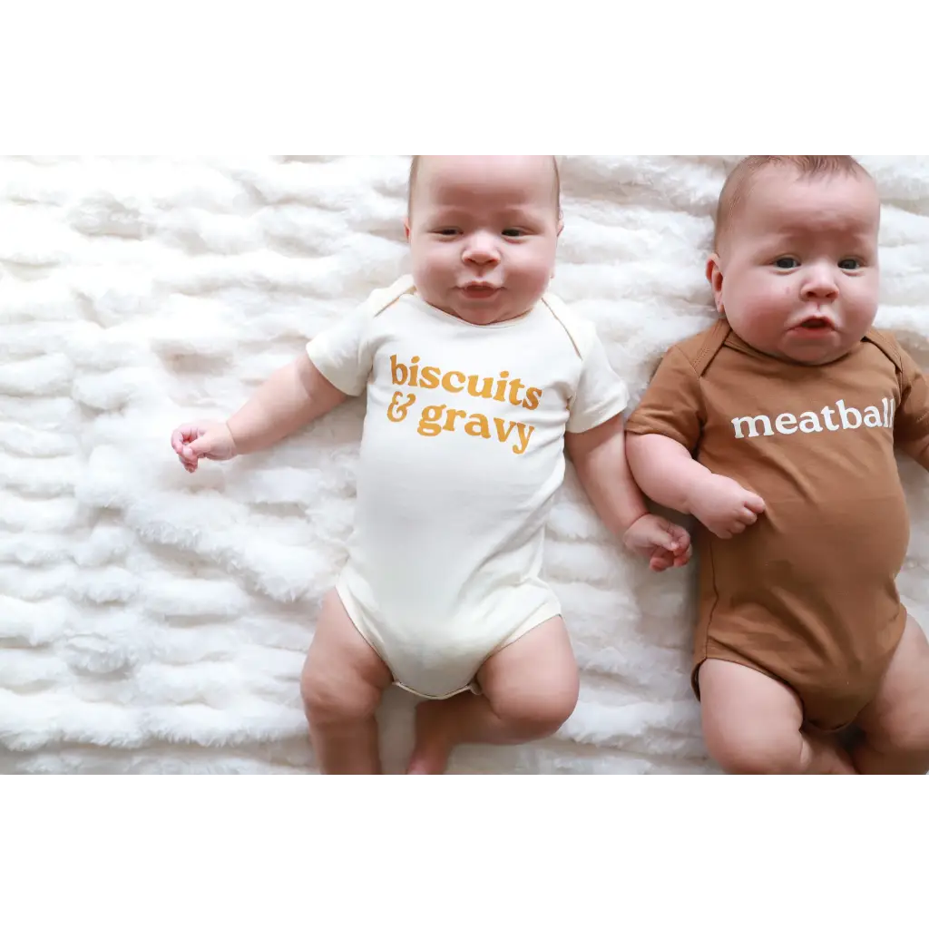 Two babies in stylish organic cotton onesies with polished prints saying biscuits n’ gravy and meatball