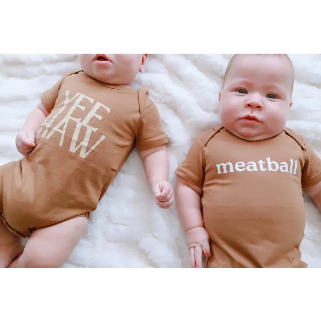 Two adorable babies in brown organic cotton onesies with polished prints, Yee Haw and Meatball