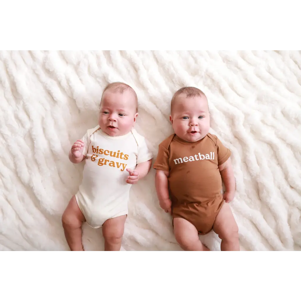 Two babies in coordinating organic cotton food-themed onesies, looking adorable together