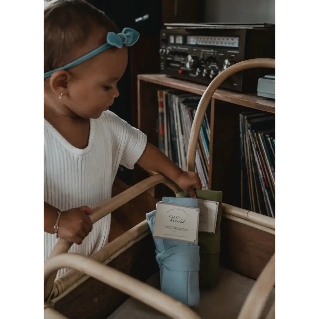 Child in white shirt and turquoise headband exploring vinyl records with mini cozy blanket