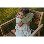 Child in a white dress on a wooden chair with a Mini Cozy Organic Cotton blanket