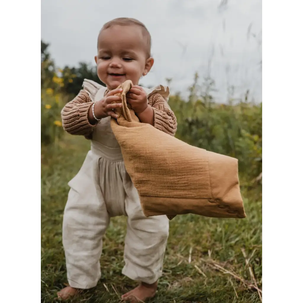 Smiling baby in beige sweater and white overalls with Mini Cozy Organic Cotton Blanket