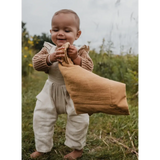 Smiling baby in beige sweater and white overalls with Mini Cozy Organic Cotton Blanket