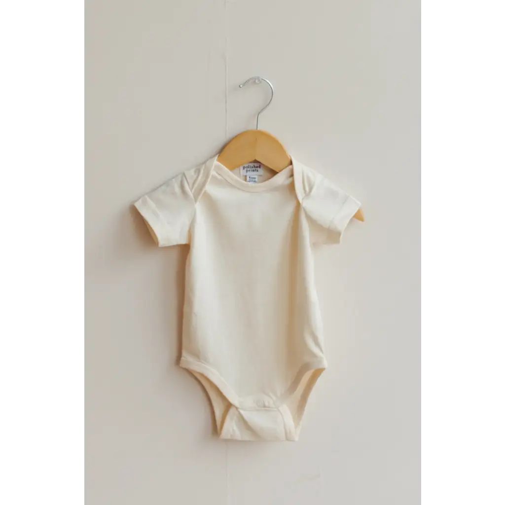 Cream-colored organic cotton baby bodysuit on a wooden hanger for your little one