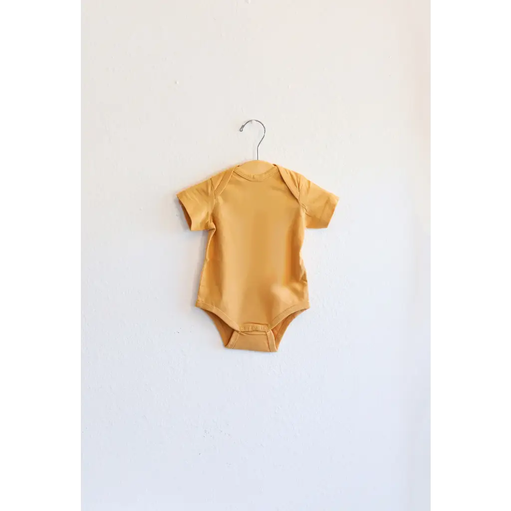 Yellow Oak Bluff baby bodysuit hanging on a hanger, made from organic cotton