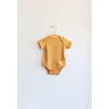 Yellow Oak Bluff baby bodysuit hanging on a hanger, made from organic cotton