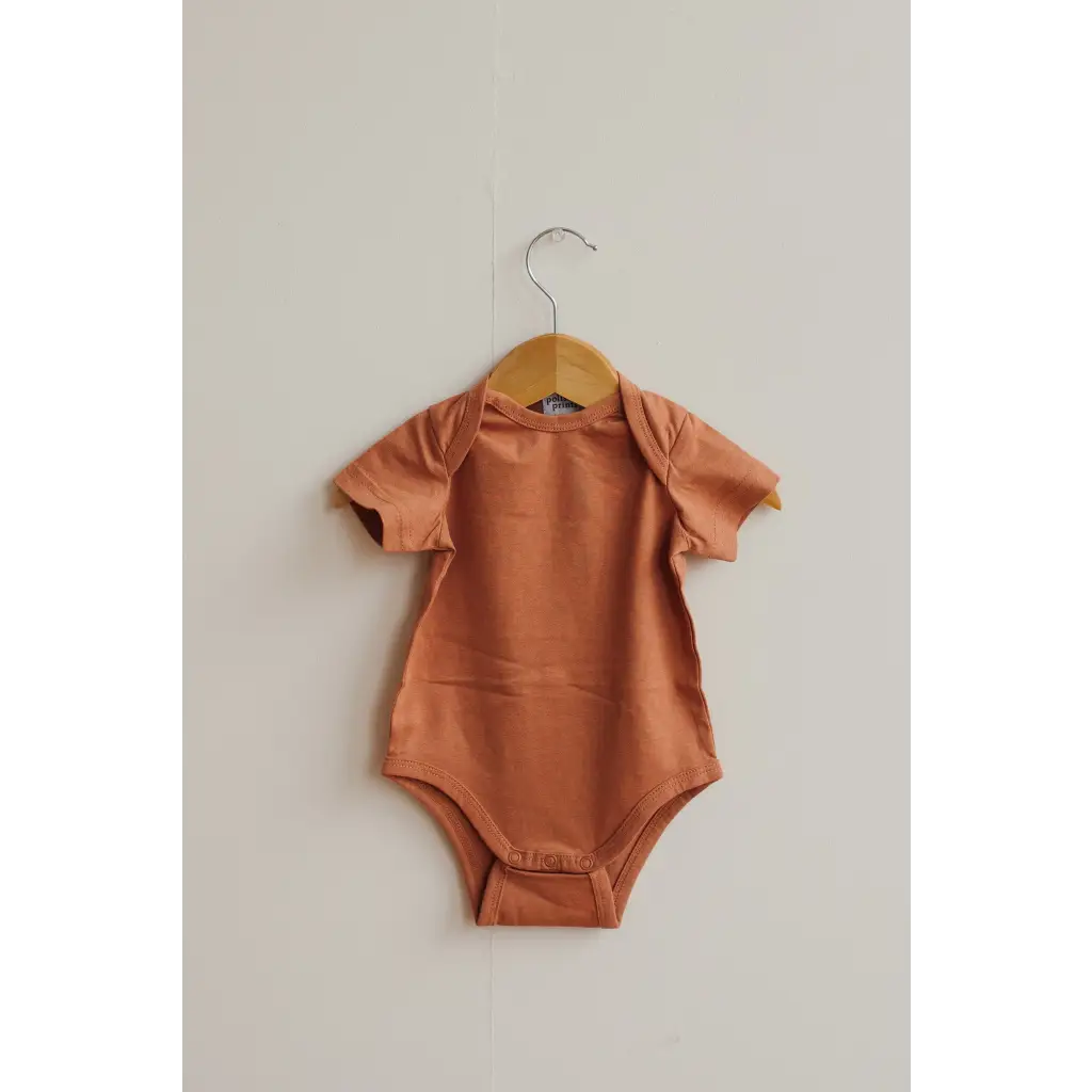 Terracotta baby bodysuit in Toasted Nut on a wooden hanger, made from organic cotton