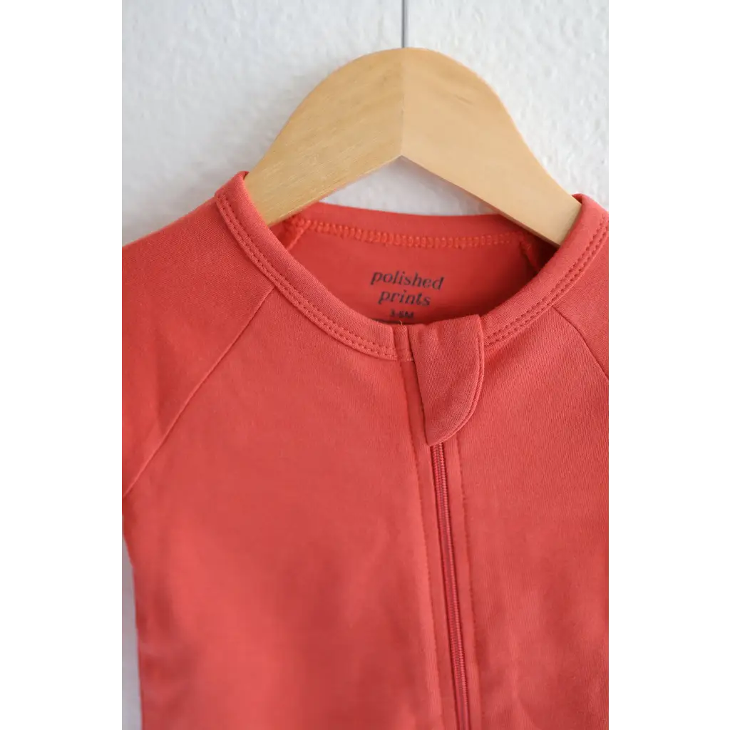Coral Organic Cotton Baby Zipper Sleeper hanging on a wooden hanger for cozy comfort
