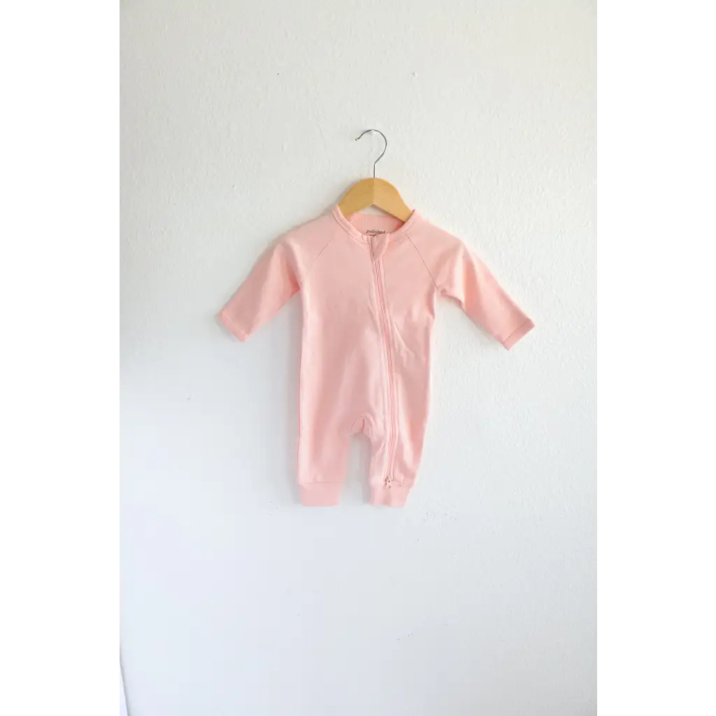 Pink Organic Cotton Baby Zipper Sleeper hanging on a wooden hanger in earthy colors