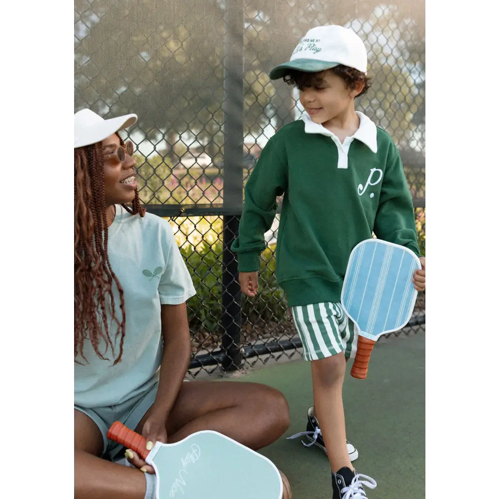 Two people on a tennis court with kids embroidered polo and pickleball paddles