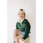 Kid in green embroidered polo pullover and denim shorts sitting on cube, stylish look