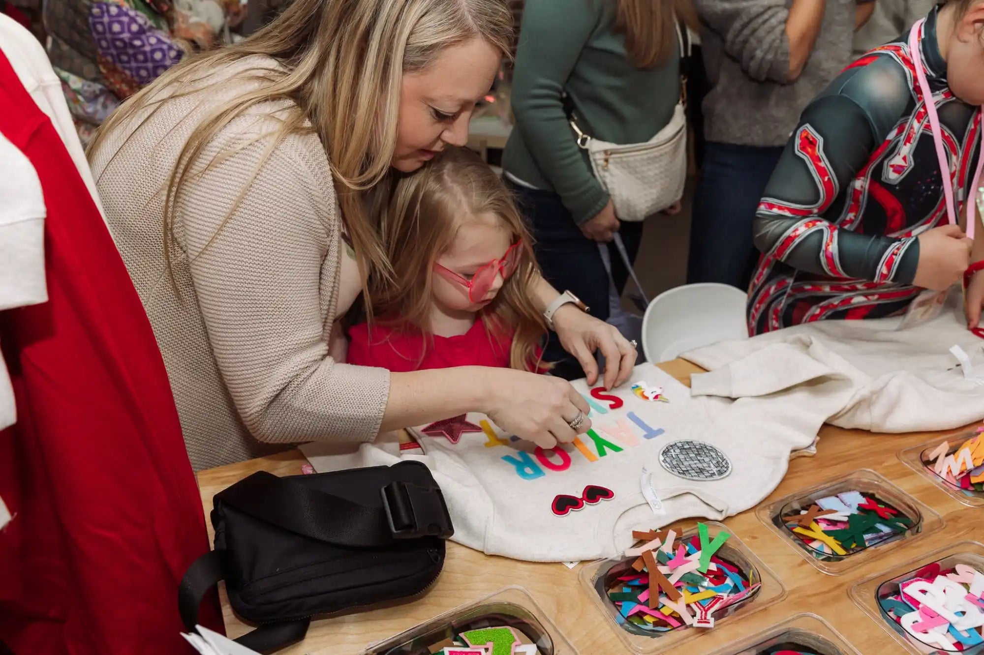 A parent and child working together on a colorful craft project at a table with art supplies.