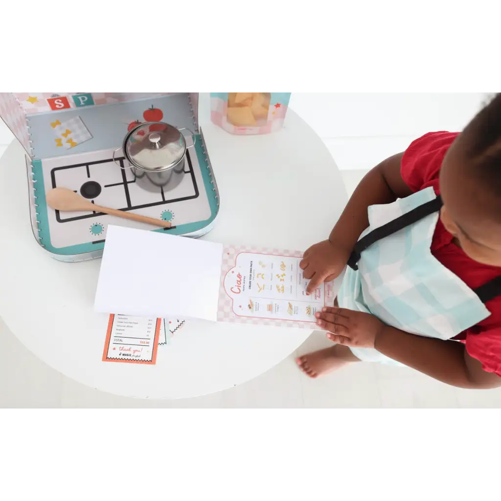 A kid using the Pasta Shop Play Kit for pretend play while drawing nearby a stovetop