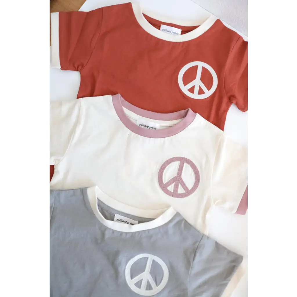 Three peace embroidered ringer tees in rust red, white, and gray for kids