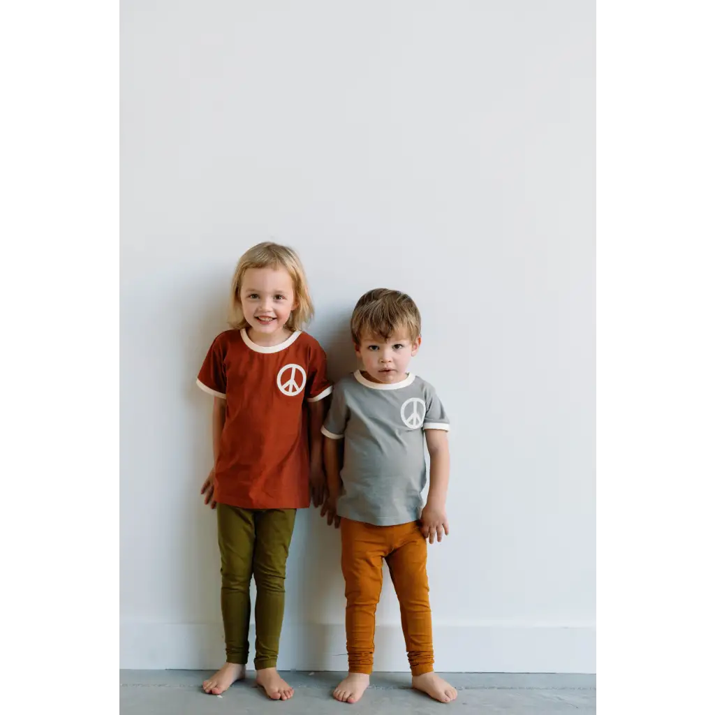 Two kids in peace embroidered ringer tees and colorful pants standing barefoot