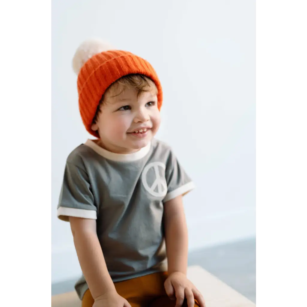 Smiling kid in a bright orange beanie and peace embroidered ringer tee