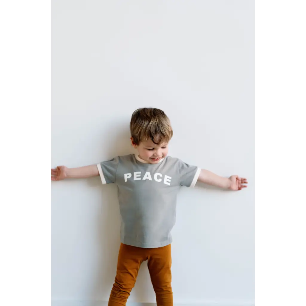 Child in gray PEACE t-shirt and brown pants showcasing Retro-inspired Everyday Ringer Tee