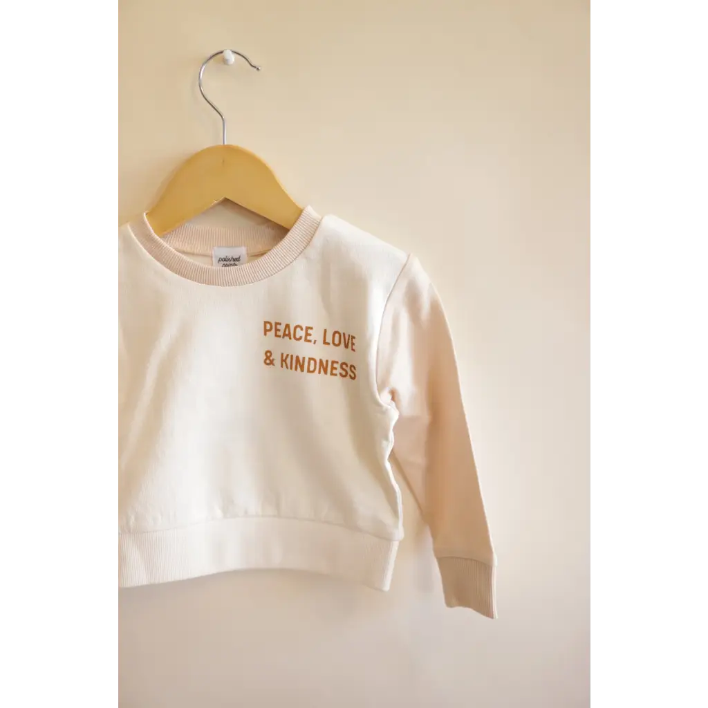 White Peace Love Kindness Pullover in Organic Cotton for Kids hanging on a hanger