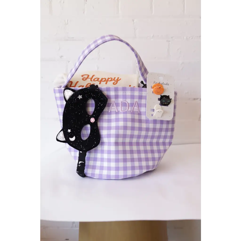 Purple gingham Halloween basket with black cat mask and spooky pins for stylish womens clothes
