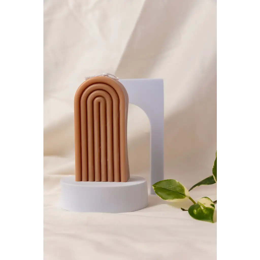 Terra cotta arch sculpture with grooves next to a Petite Rainbow Candle for colorful vibes