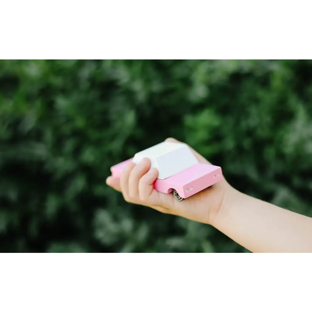 Hand holding a pink and white eraser next to a Bubble Gum Pink Sedan in Solid Beech Wood