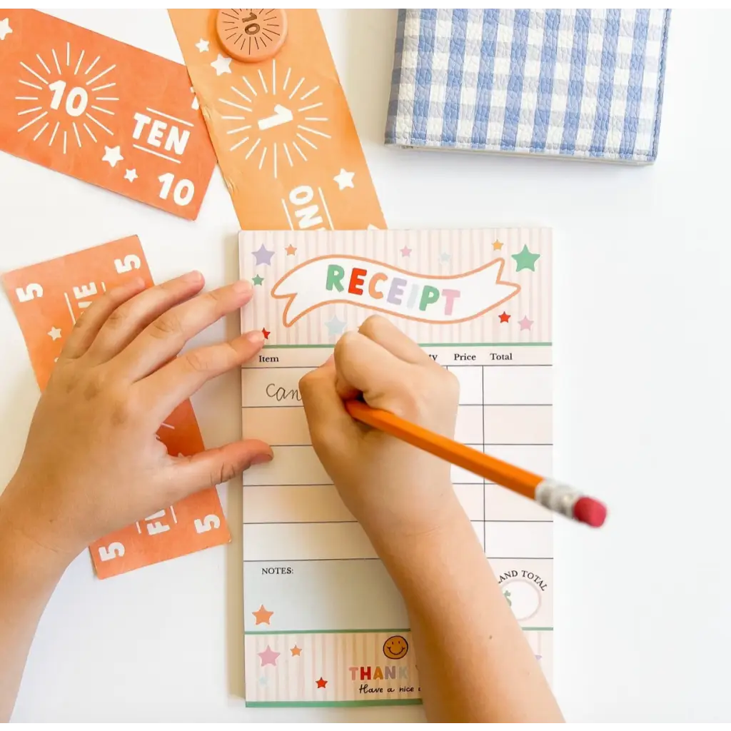 Hands writing on a pretend play receipt with orange number cards for creative kids