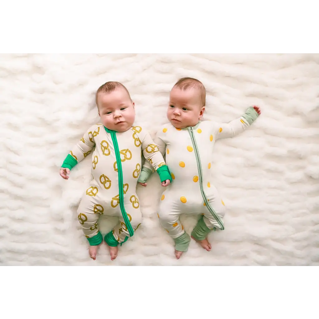 Twin babies in matching yellow and green onesies, cozy in Pretzel Party Bamboo Baby Sleeper