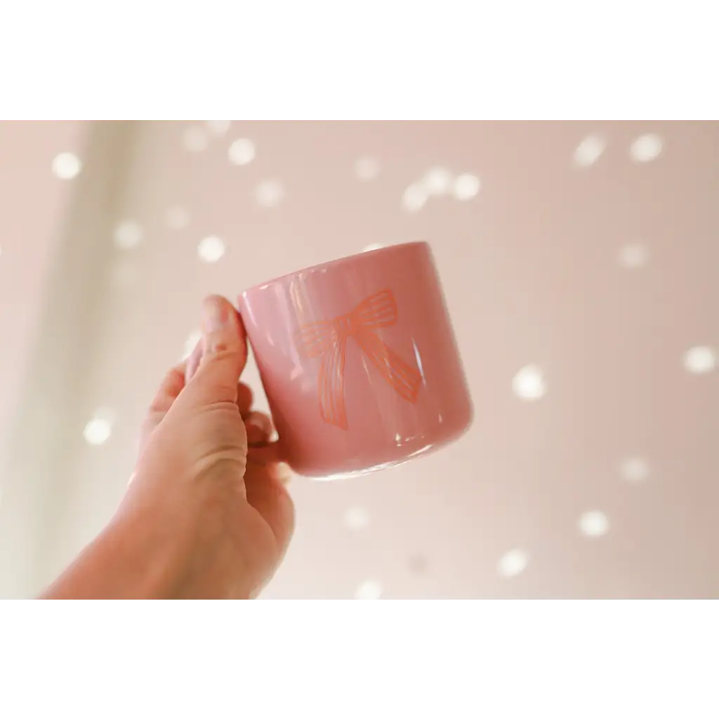 Hand holding a pink ceramic mug with a cute bow design, perfect campfire mug