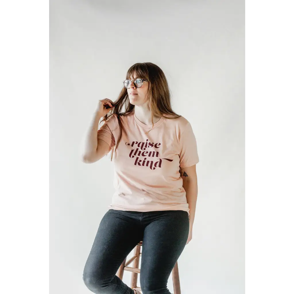 Pink graphic t-shirt with Raise Them Kind text, made from soft organic cotton